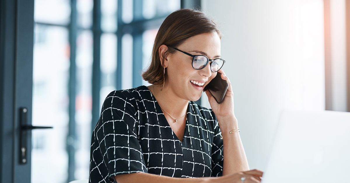 An woman makes a phone call while working on her computer